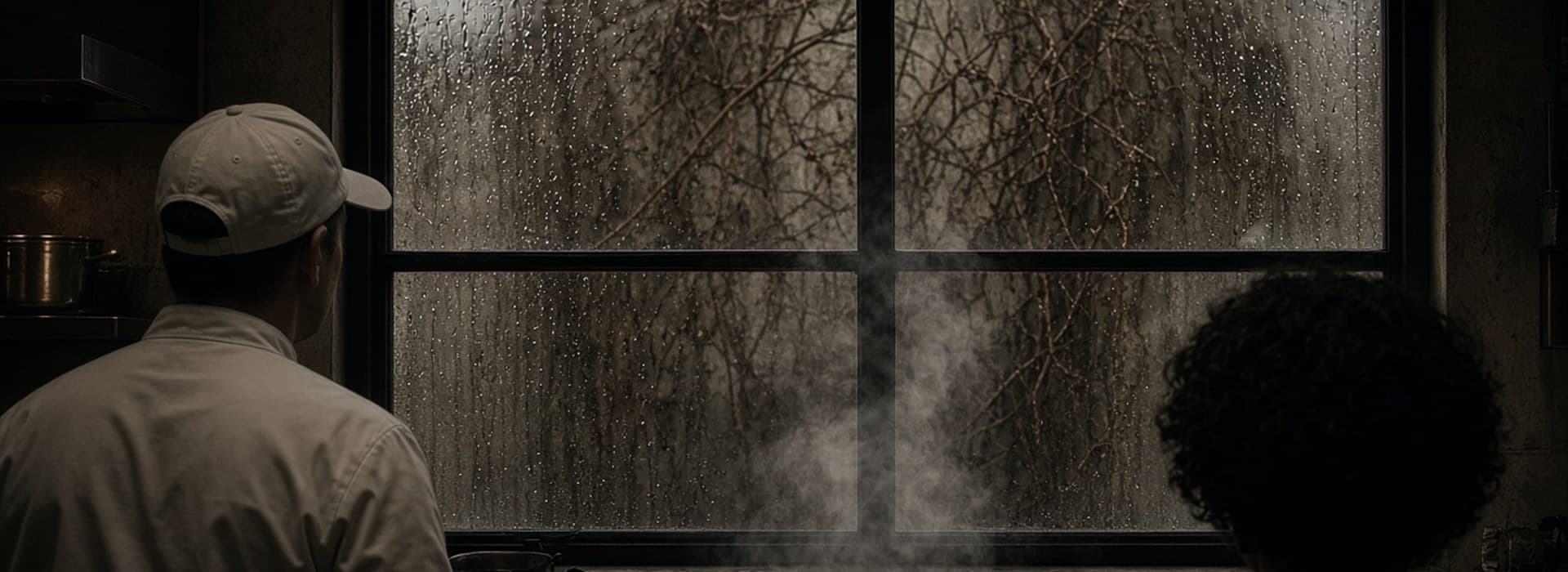 Chef and colleague looking out a rain-streaked kitchen window